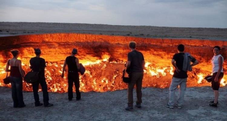 Reizigers staan aan de rand van de vurige Darvaza gaskrater die gloeit met vlammen bij schemering.
