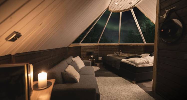 Gezellige zolderslaapkamer met glazen plafond dat het noorderlicht in de nachtelijke hemel onthult.