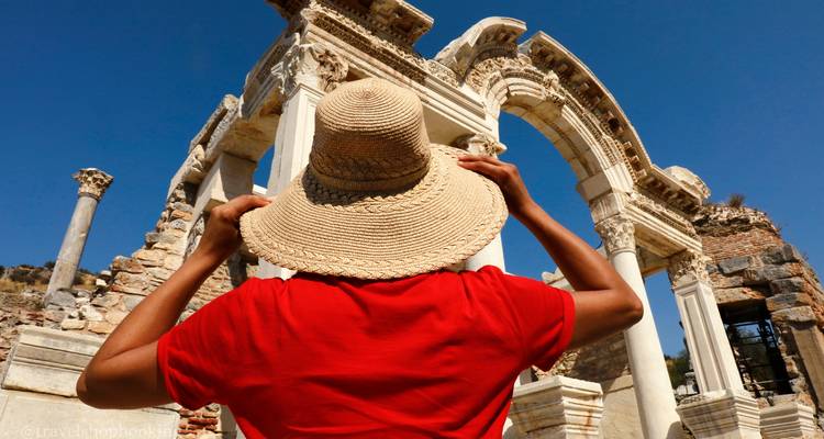 Vista trasera de una mujer con camisa roja y sombrero de paja admirando los arcos de mármol del Templo de Adriano en Éfeso.