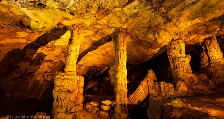 Interior de cueva iluminada con dramáticas estalactitas y estalagmitas en cálida iluminación dorada.