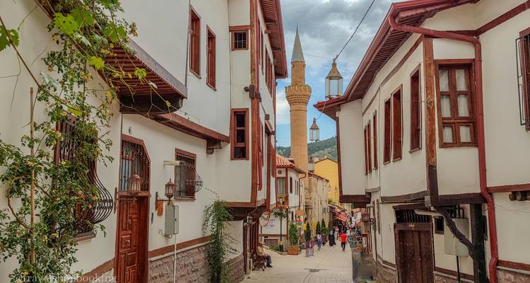 Encantadora calle otomana estrecha bordeada de casas blancas de madera y un minarete distante; turistas pasean abajo.