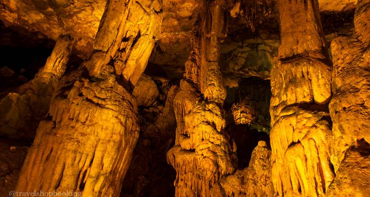 Formaciones verticales de cueva que brillan en ámbar dentro de una caverna iluminada.