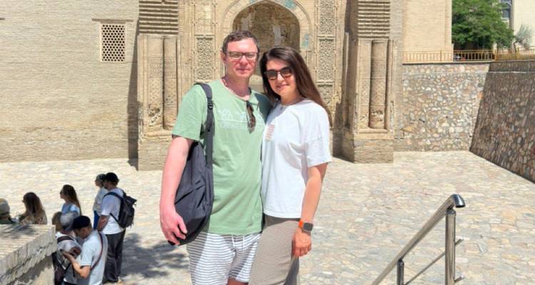 Stel poseert voor een ingewikkeld gesneden portaal van een historische madrassa op een zonnige middag.