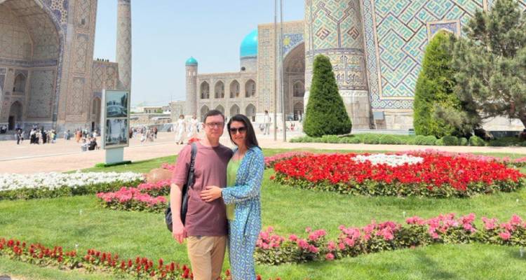 Jong stel staat te midden van kleurrijke bloemperken met de monumentale madrasas van Registan die erachter oprijzen.