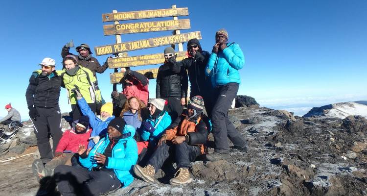 Escaladores victoriosos celebran en el letrero de Uhuru Peak en la cumbre cubierta de nieve del Kilimanjaro bajo cielos despejados.