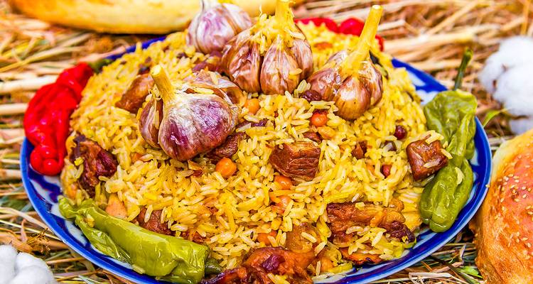 Plato vibrante de plov de Asia Central apilado alto con arroz, cordero, garbanzos, bulbos de ajo y pimientos.