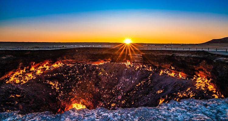 El sol se pone en el horizonte proyectando rayos sobre las profundidades ardientes del cráter en llamas de Darvaza.