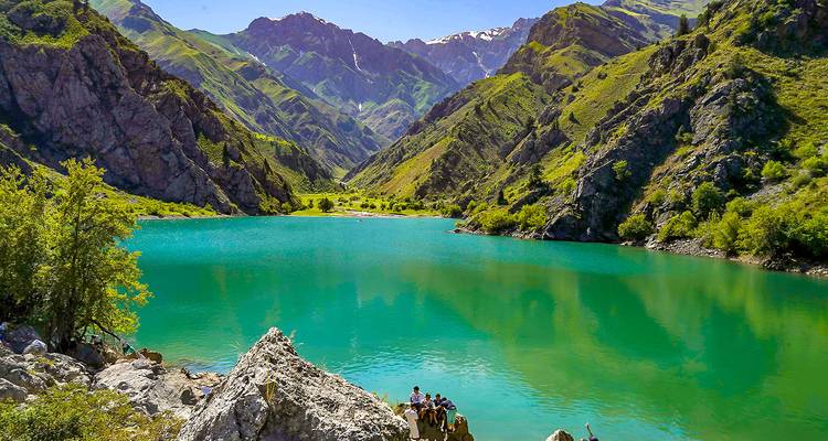 Lago alpino turquesa rodeado de montañas verdes empinadas y picos nevados bajo un cielo despejado.