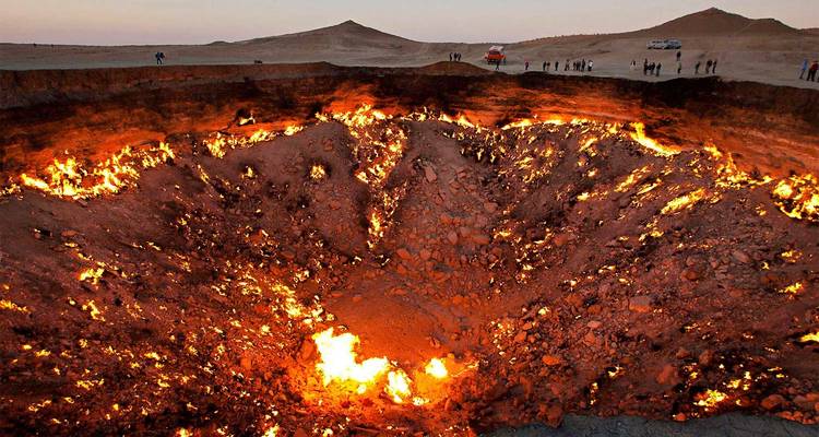 Le cratère de gaz de Darvaza ardent, resplendissant de flammes à l'intérieur d'un vaste gouffre désertique au crépuscule.