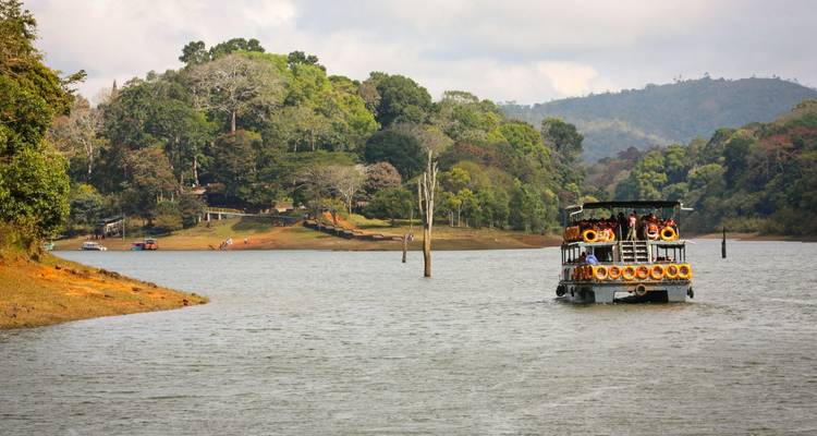 Rondvaartboot die vaart over een rustig bosmeer met heuvels op de achtergrond