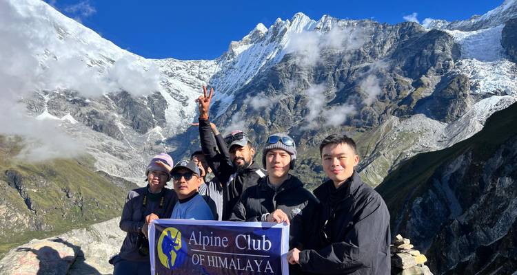 Eine Trekkinggruppe hält ein Alpenverein-Banner mit schneebedeckten Himalaya-Gipfeln, die sich hinter ihnen erheben.