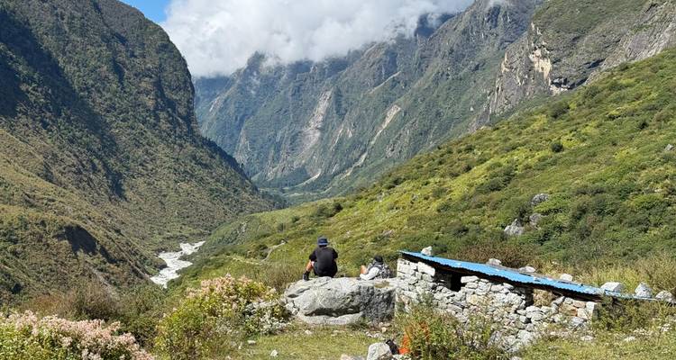 Wanderer ruht auf einem Felsblock mit Blick auf ein tiefgrünes Tal, das von einem Gletscherfluss im Himalaya geformt wurde.