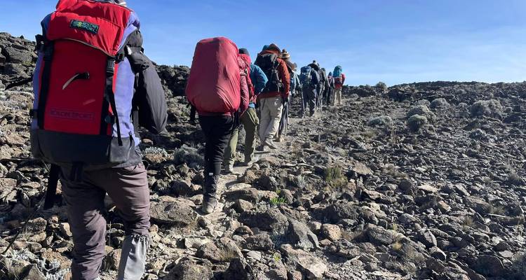 Des randonneurs avec de gros sacs à dos marchent en file indienne sur un versant alpin rocheux.