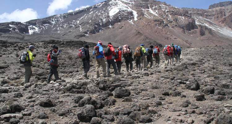 Une longue file de randonneurs traverse une vallée volcanique aride sous la crête sommitale du Kilimandjaro.