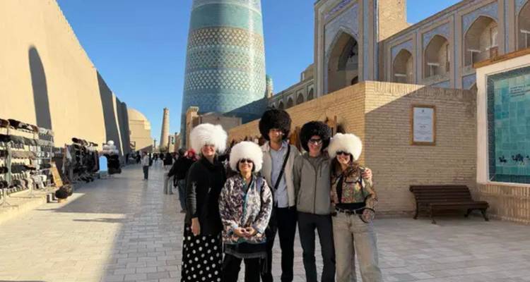 Reizigers in pluizige witte hoeden poseren op een zonovergoten straat naast Khiva's turquoise minaret.