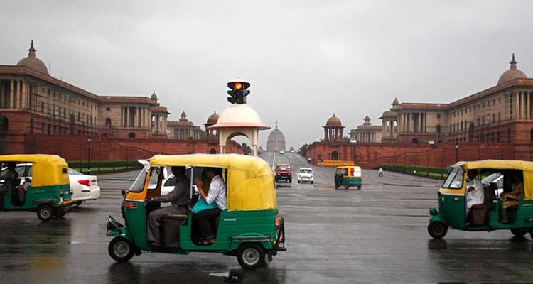 Des auto-rickshaws roulent sur le large boulevard bordé par les bâtiments du Secrétariat en grès rouge de New Delhi par une journée nuageuse.