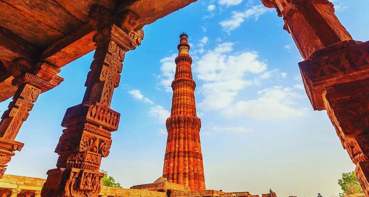 Le Qutub Minar qui s'élance, encadré par des piliers de grès finement sculptés sous un ciel d'un bleu éclatant.