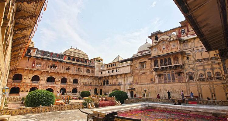 Grande cour de palais du Rajasthan avec bassin fleuri, arcades et visiteurs explorant.