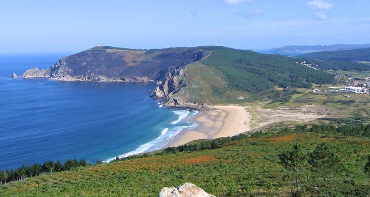 Vista panorámica de un promontorio verde escarpado y una playa de arena apartada en la costa gallega