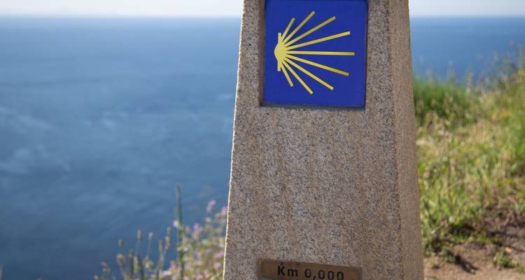 Marcador de piedra del kilómetro cero del Camino de Santiago con emblema de concha de vieira con vista al mar