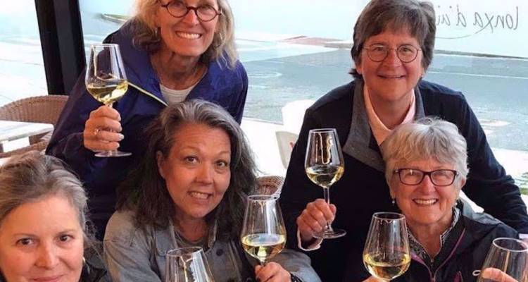 Mujeres sonrientes levantando copas de vino blanco en un café al aire libre