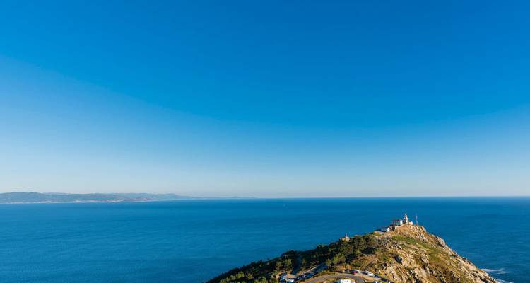 Vista aérea de la península del Cabo Finisterre adentrándose en el Atlántico azul profundo bajo un cielo despejado