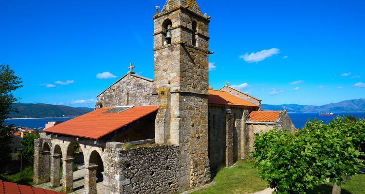 Iglesia románica de piedra con campanario con vistas al mar azul y las montañas en Galicia