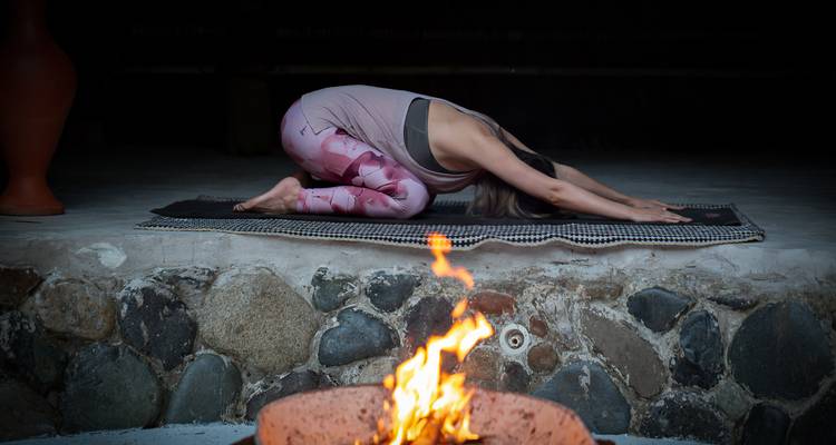 Femme pratique la pose de l'enfant du yoga sur un tapis devant un foyer qui crépite