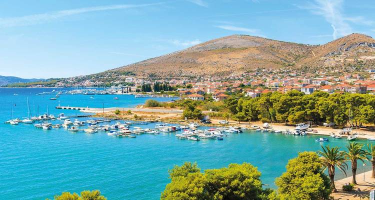 Une pittoresque ville côtière croate avec une marina de bateaux blancs se trouve au bord d'une eau turquoise et de collines arides.