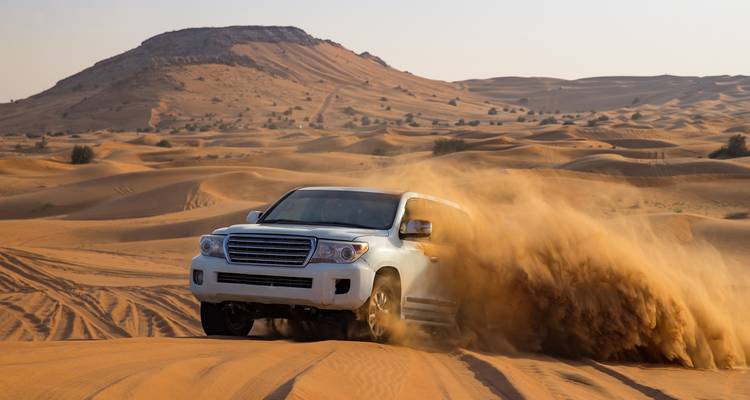 SUV levantando una dramática nube de arena mientras acelera a través de las dunas del desierto.