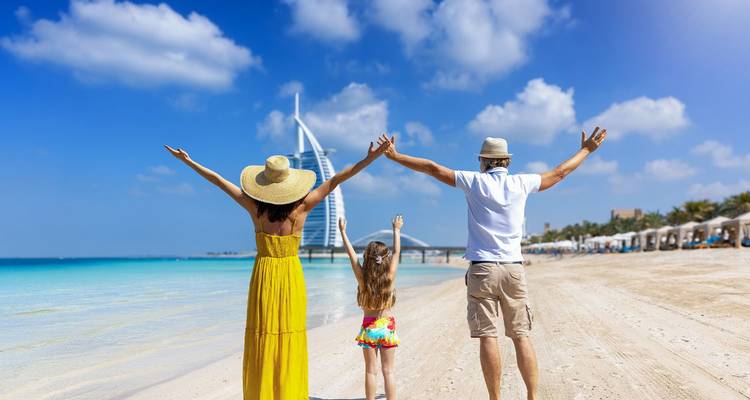 Familie steekt armen in de lucht van vreugde op een ongerepte Dubai-strand met turquoise zee en de Burj Al Arab in de verte.