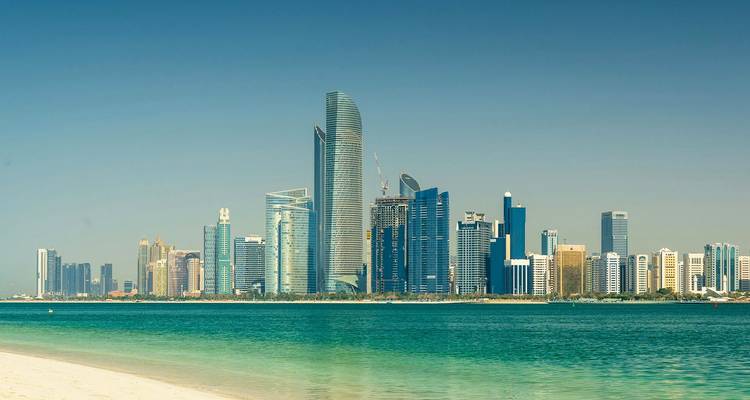 De moderne skyline van Abu Dhabi rijst uit op een heldere dag boven het turquoise water van de Golf.