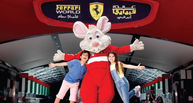 Kinderen poseren met Ferrari World's cartoon muis mascotte onder de rode toegangsboog.