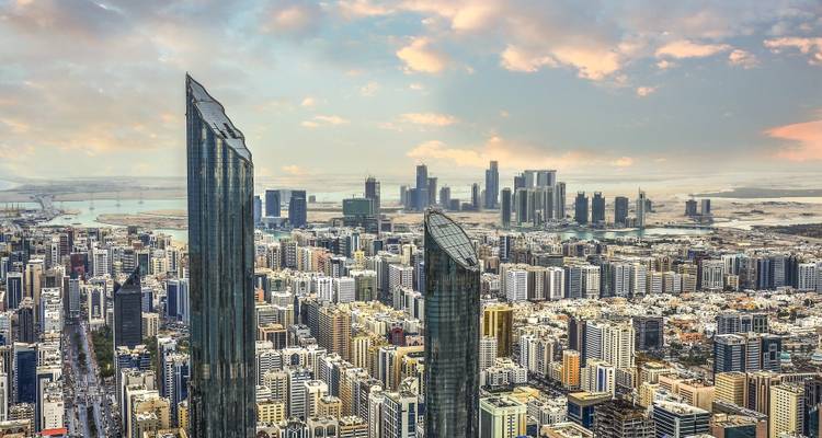 Bovenaanzicht van Abu Dhabi's moderne skyline met hoge glazen torens en uitgestrekt stadsraster bij zonsopgang.