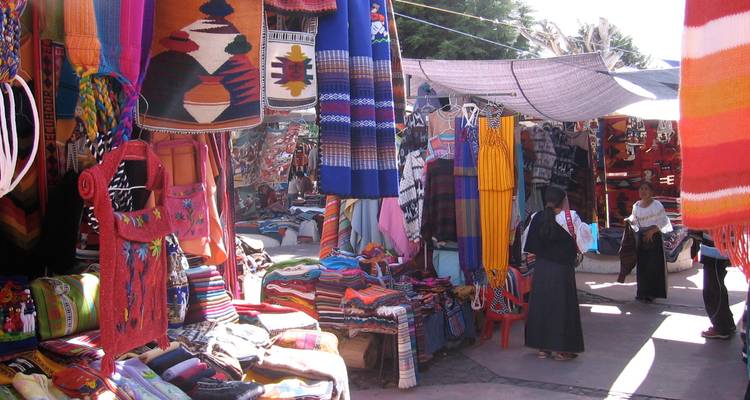 Farbgetränkte Gänge des Otavalo-Marktes mit Decken, Ponchos und Käufern unter provisorischen Planen.