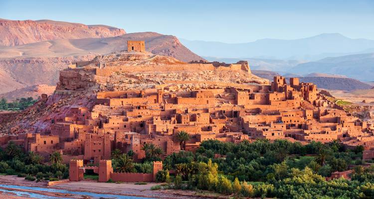 Antiguo ksar de adobe de Ait Benhaddou elevándose sobre un oasis verde con montañas al fondo