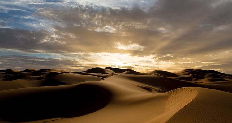 Las infinitas dunas de arena del Sahara brillando al amanecer bajo un cielo dramático iluminado por nubes.