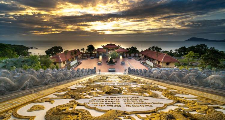 Complexe de pagodes au sommet d'une colline surplombant la mer au coucher de soleil dramatique avec des sculptures de dragons encadrant l'escalier au premier plan sur l'île de Phu Quoc