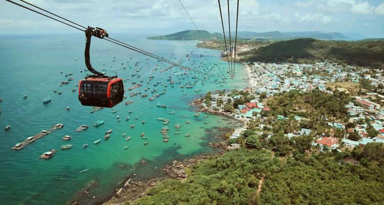 Une cabine de téléphérique rouge glisse haut au-dessus des eaux turquoise et d'un village de pêcheurs sur la côte de l'île de Phu Quoc