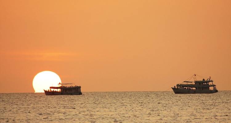 Scène de coucher de soleil minimaliste avec deux bateaux de pêche en silhouette contre un horizon orange lumineux.