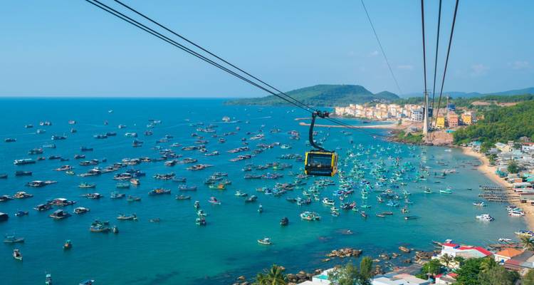 Cabine de téléphérique voyageant au-dessus d'une vaste flotte de bateaux de pêche sur des eaux d'un bleu éclatant.