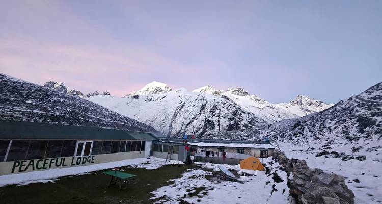 Sneeuwbedekte berghut en tenten onder roze schemerluchten met hoge bergtoppen op de achtergrond.