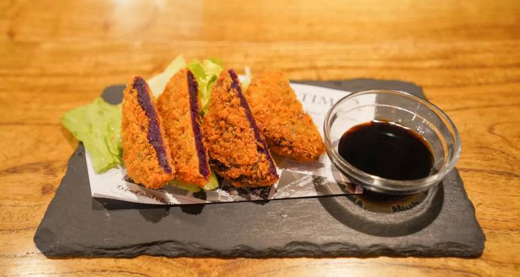 Tranches de sandwich frit japonais servies sur ardoise avec sauce pour trempage.