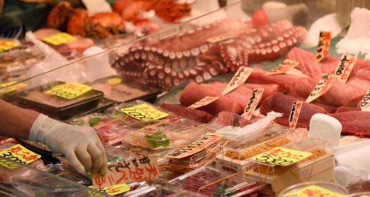 Étal animé du marché aux fruits de mer affichant du thon frais, du poulpe et des étiquettes de prix.