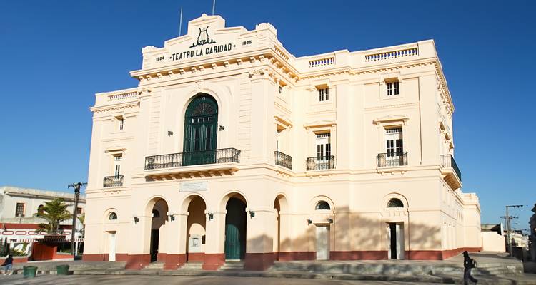 Elegantes cremefarbenes neoklassizistisches Theatergebäude unter klarem blauen Himmel.