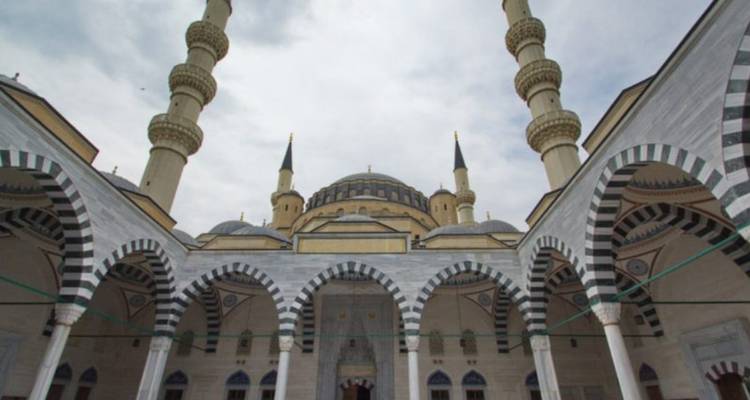 Cour de mosquée en marbre blanc grandiose avec des minarets jumeaux s'élevant dans un ciel nuageux.