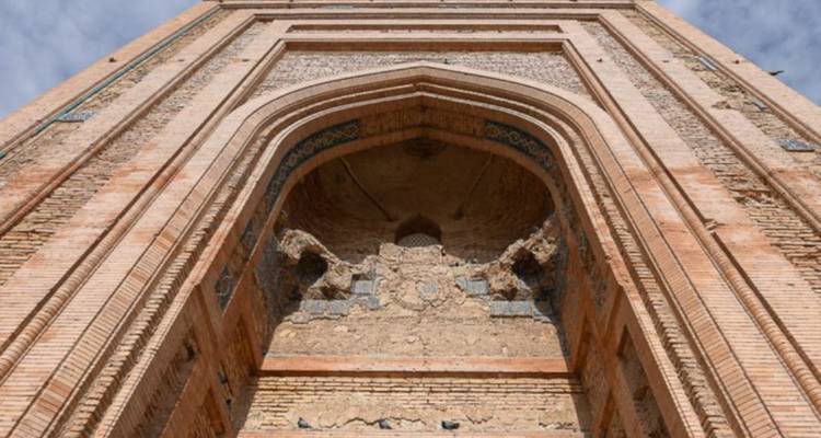 Vue en contre-plongée d'une arche en brique ornementée et de la façade imposante d'un ancien minaret ou portail.