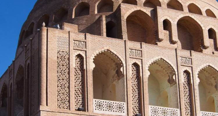 Vue détaillée d'un mausolée en brique présentant des fenêtres voûtées ornées et des motifs géométriques islamiques.