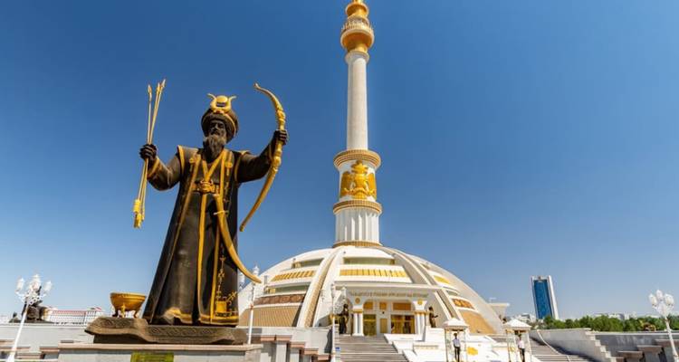 Statue dorée d'un guerrier et colonne imposante blanche et dorée du Monument de la Neutralité à Achgabat sous un ciel dégagé.