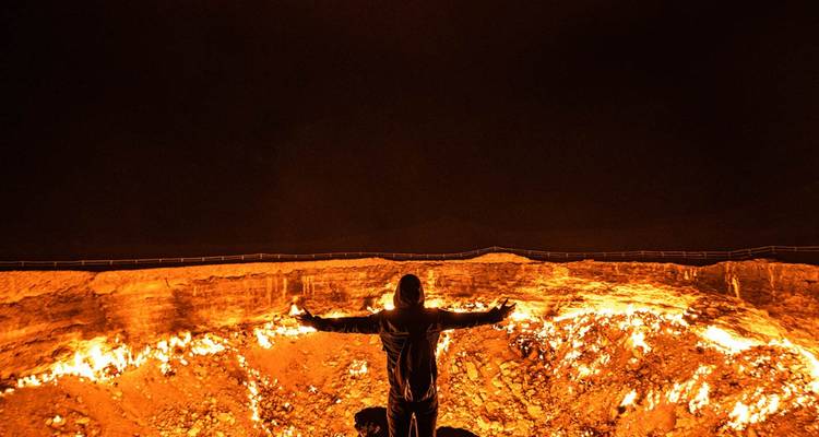 Reisender steht triumphierend vor dem glühenden Darvaza-Krater unter einem pechschwarzen Himmel.